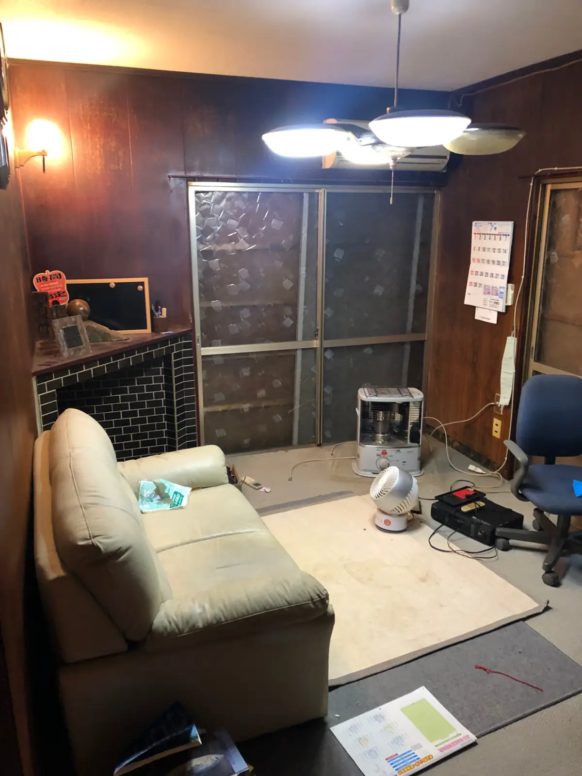 Living room before renovation, with dark wood panelling, an old sofa and worn carpet