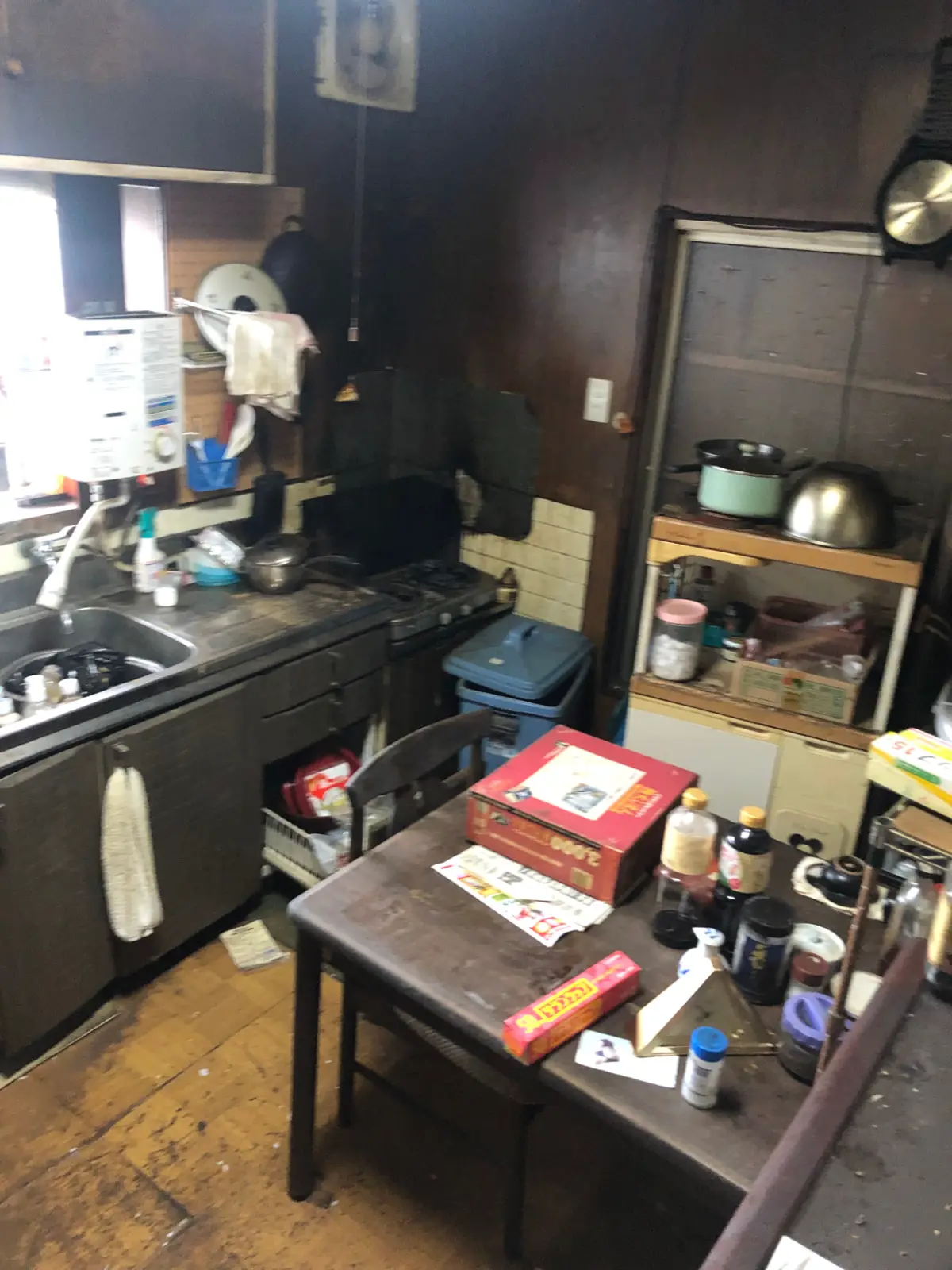 Kitchen before renovation, with dark timber walls, an old sink unit and clutter across the worn floor