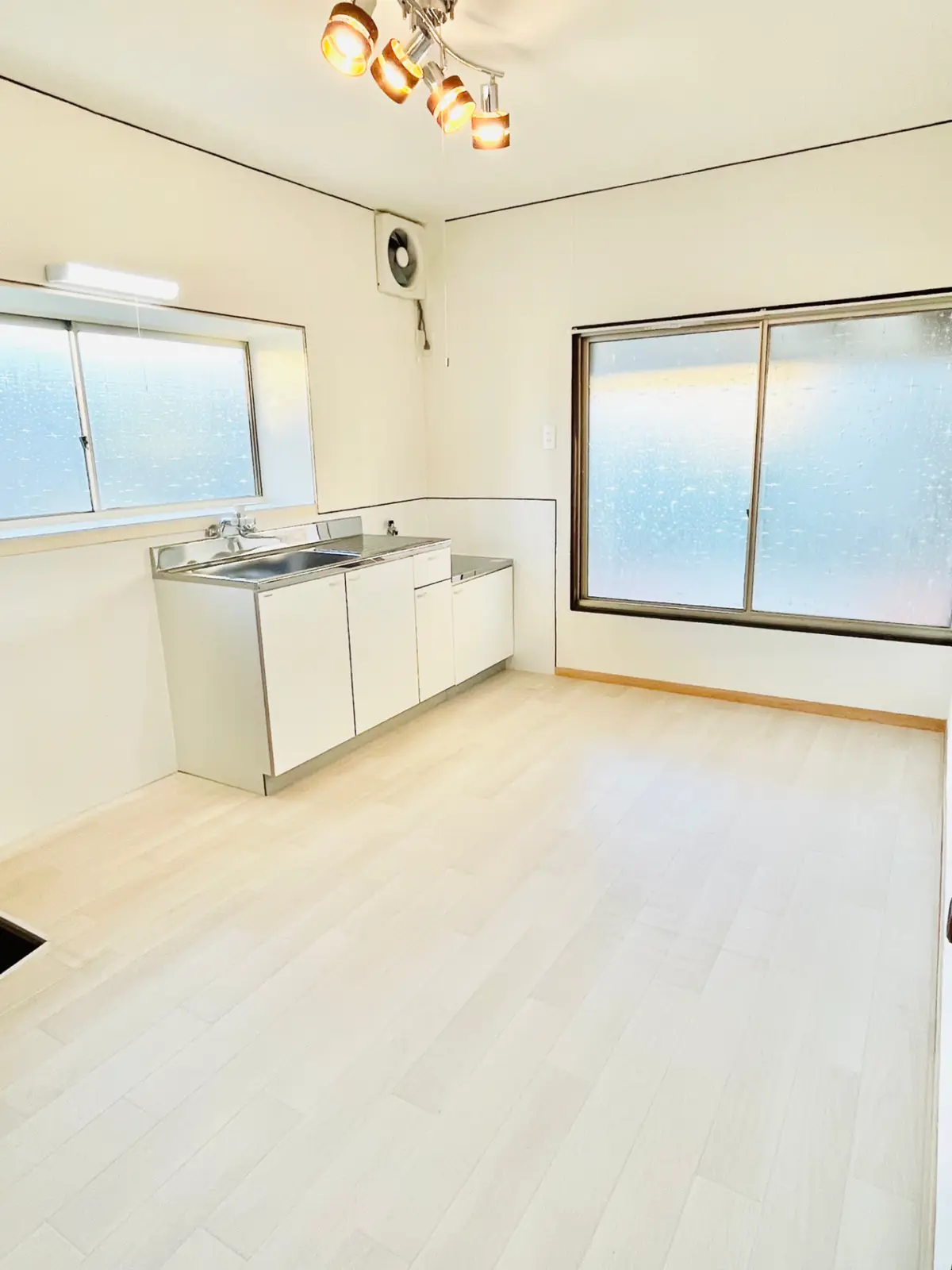 The same kitchen after renovation, with white walls, pale new flooring and a clean sink and counter unit