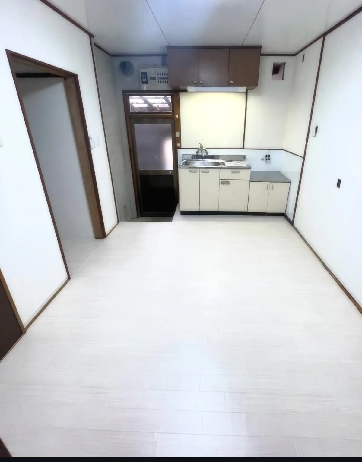The same kitchen after renovation, with pale new flooring, clean white walls and a tidy sink unit