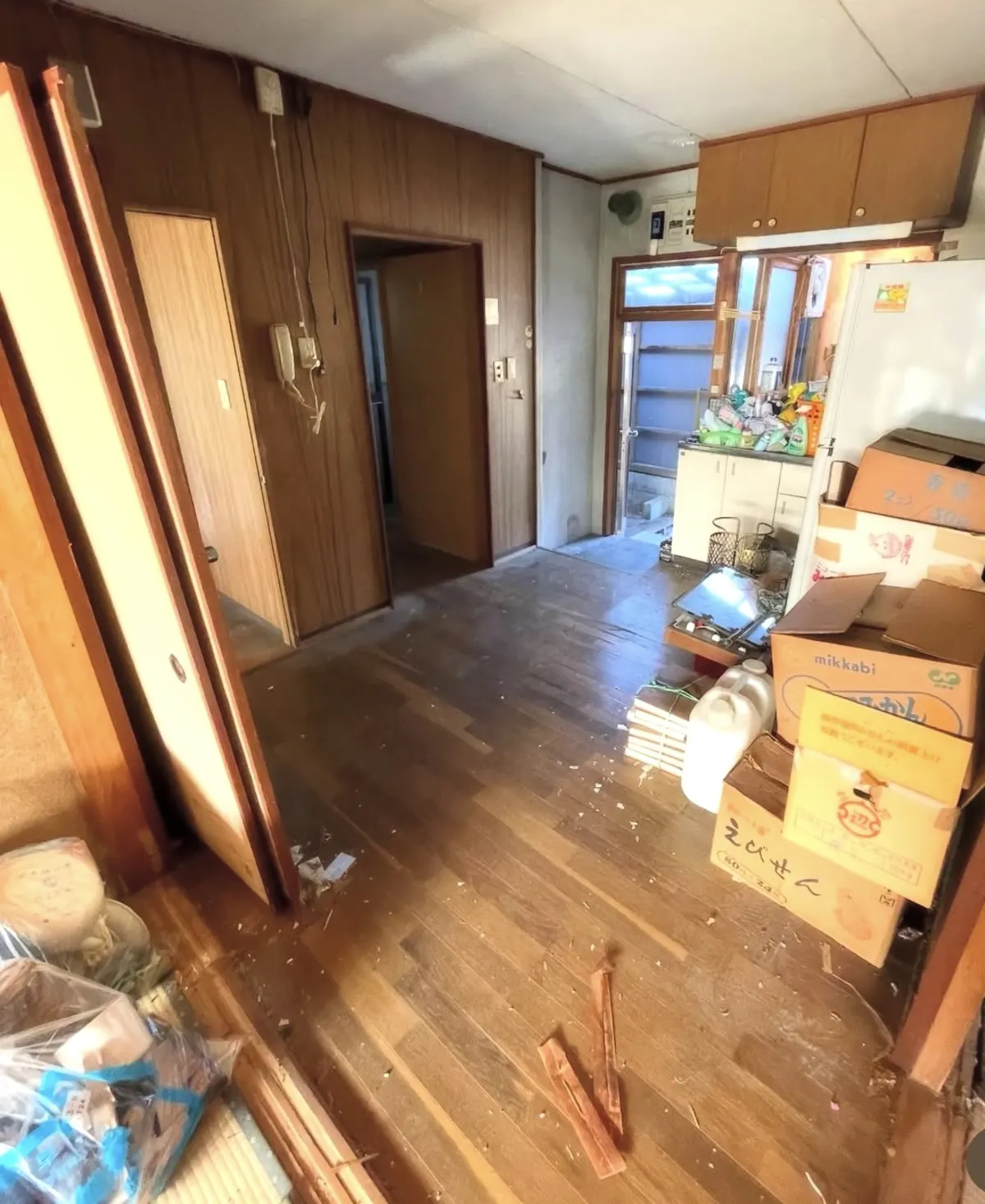 Kitchen before renovation, with dark wood panelling, worn flooring and boxes stacked against the wall